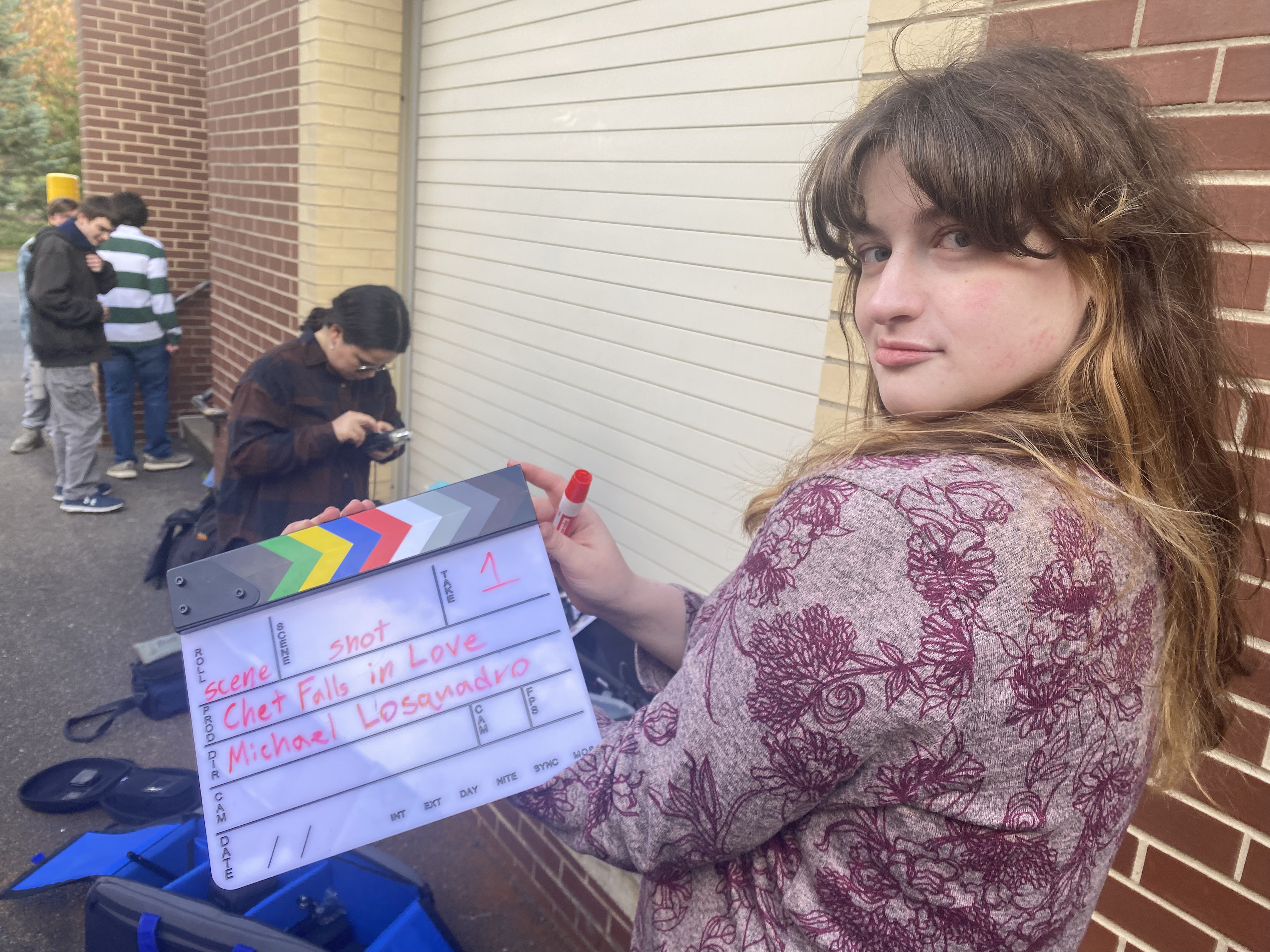 Corrine looking smugly towards the camera holding the slate for Chet Falls in Love, she knows she's the number 1 slatest in america